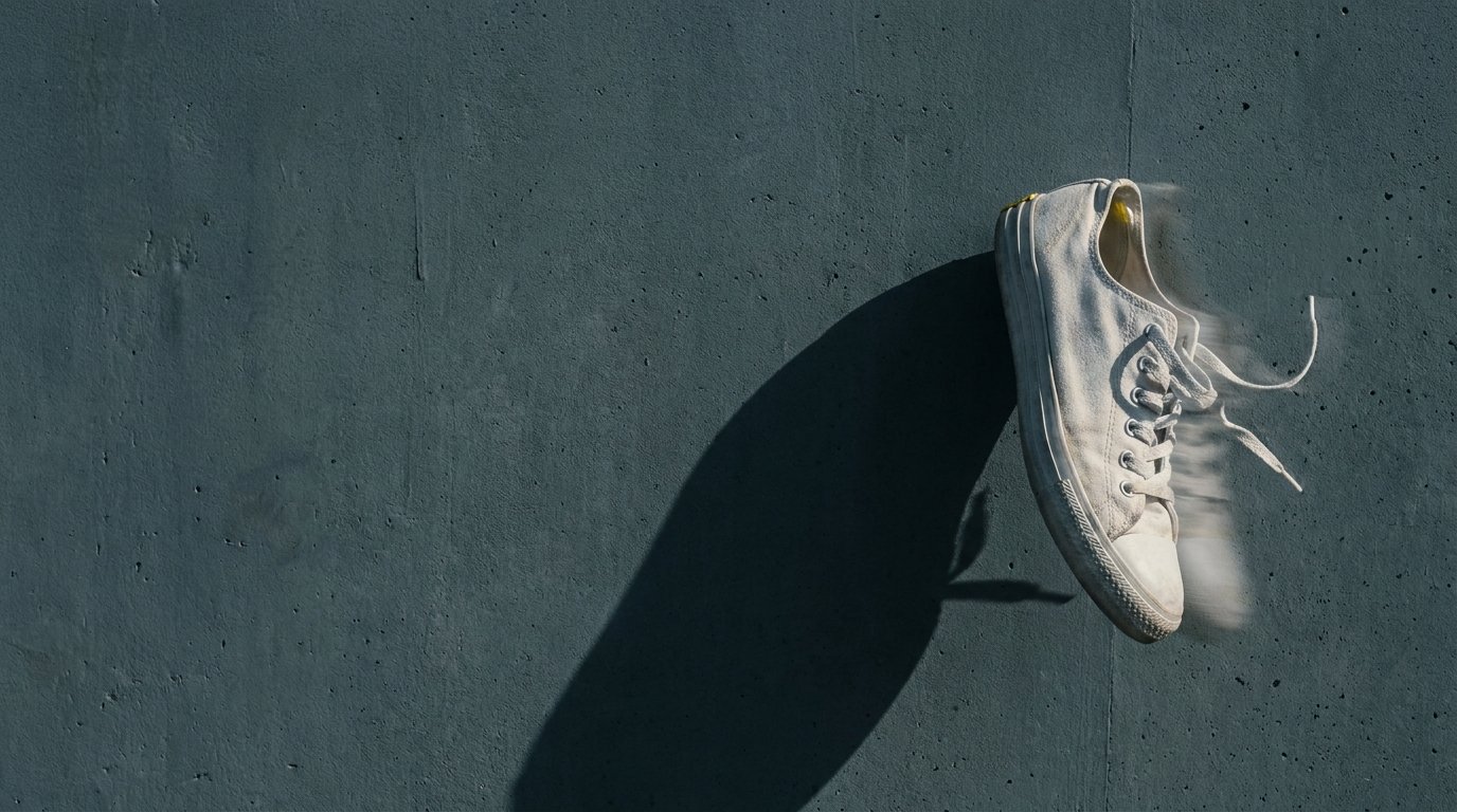 A single white sneaker mid-stride frozen against concrete, long shadow.